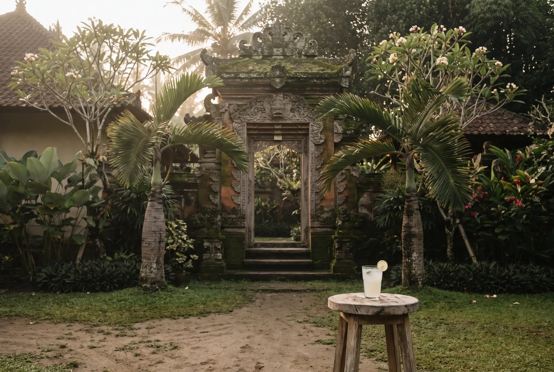 A carved Balinese gateway at an Ubud villa in golden morning light, a welcome drink waiting