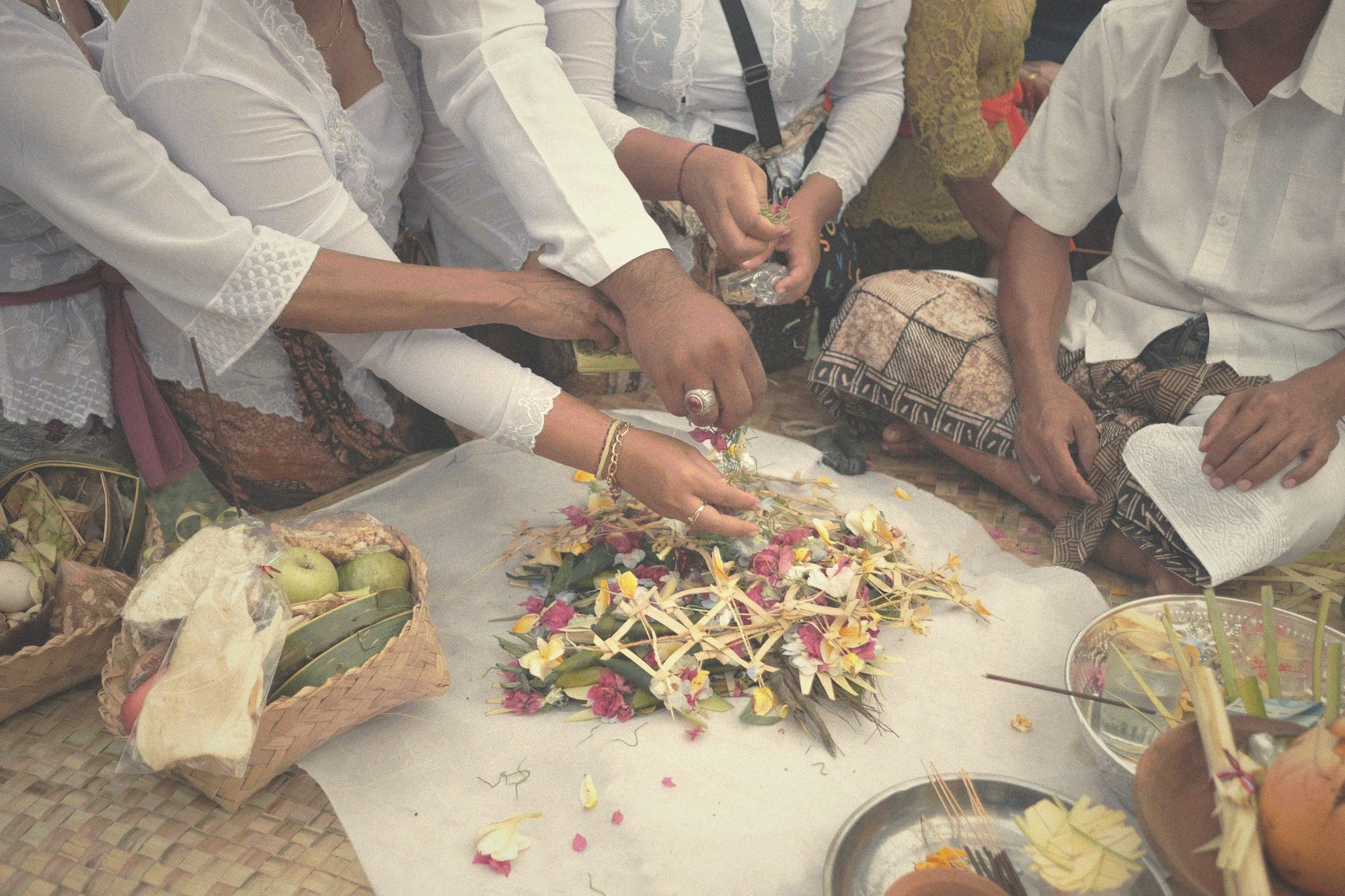 Anonymous hands arranging canang sari flower offerings on a white cloth