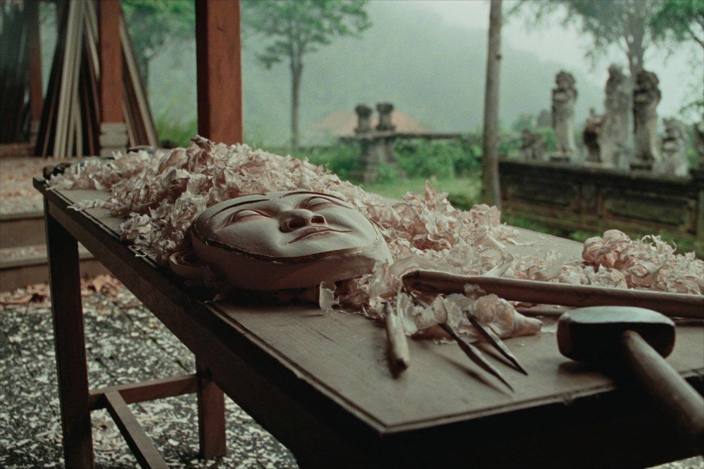 A carved topeng mask emerging from a wood block in Mas